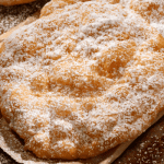 Golden, freshly fried dough sprinkled with powdered sugar, perfect for recreating a classic fairground dessert at home.