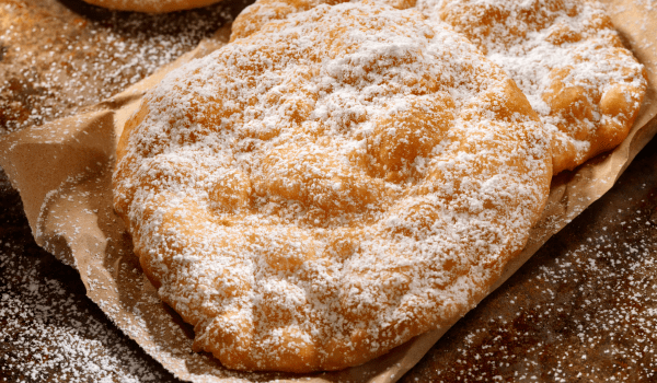 Golden, freshly fried dough sprinkled with powdered sugar, perfect for recreating a classic fairground dessert at home.