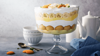 A full view of a glass bowl featuring traditional Southern banana pudding layers: vanilla wafers, fresh banana slices, creamy pudding, and whipped cream, elegantly presented on a table with dessert utensils.