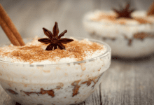 Mexican arroz con leche served in a glass bowl, decorated with a star anise and a cinnamon stick, showcasing layers of texture and color on a light wooden surface.