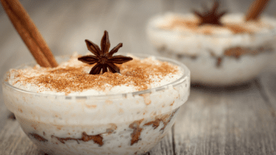 Mexican arroz con leche served in a glass bowl, decorated with a star anise and a cinnamon stick, showcasing layers of texture and color on a light wooden surface.