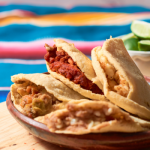 Plate of gorditas filled with various fillings like chorizo, beans, and salsa, served on a wooden table with lime wedges in the background. A colorful Mexican tablecloth adds a festive and traditional touch.