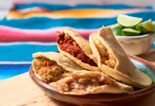 Plate of gorditas filled with various fillings like chorizo, beans, and salsa, served on a wooden table with lime wedges in the background. A colorful Mexican tablecloth adds a festive and traditional touch.