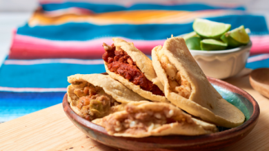 Plate of gorditas filled with various fillings like chorizo, beans, and salsa, served on a wooden table with lime wedges in the background. A colorful Mexican tablecloth adds a festive and traditional touch.