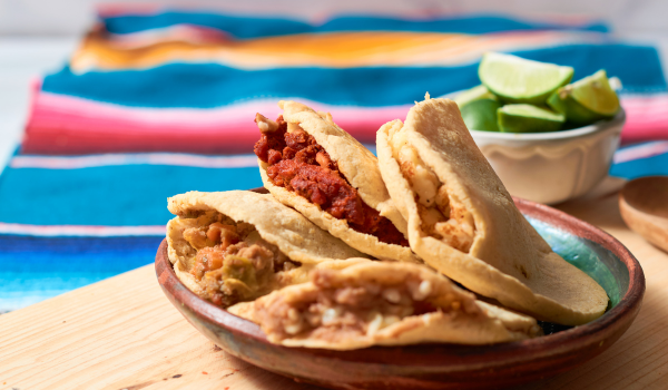 Plate of gorditas filled with various fillings like chorizo, beans, and salsa, served on a wooden table with lime wedges in the background. A colorful Mexican tablecloth adds a festive and traditional touch.