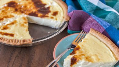 Old Fashioned Custard Pie in a glass pie dish with a golden-brown crust and rich custard filling. A slice is plated on a blue and orange plate, ready to be enjoyed with whipped cream or as is.